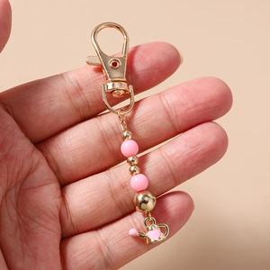 Detailed close-up of a pink beaded phone strap with a golden watering can charm
