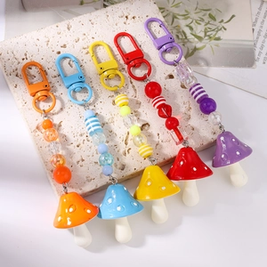 Detail showing five colorful mushroom keychains with striped beads on stone surface