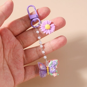 Detail eines lila Gänseblümchen-Schlüsselanhängers mit Perlenkette und Schmetterling