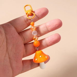 Detail of hand-held orange mushroom keychain with striped beads and a metal hook