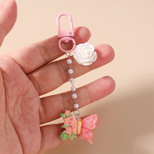 Detail eines rosa Schlüsselanhängers mit weißer Harzrose und Schmetterling am Taschenanhänger