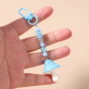 Detail showing hand holding a blue mushroom keychain with striped beads and metal clasp