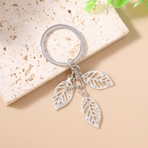 Minimalist silver leaf keychain with hollow leaf pendants on a beige stone surface