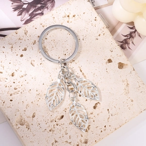 Macro detail of silver leaf keychain with three cutout pendants on a beige stone surface