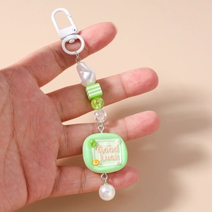 Detail of beaded keychain featuring a Good Luck charm, striped cubes, and pearls