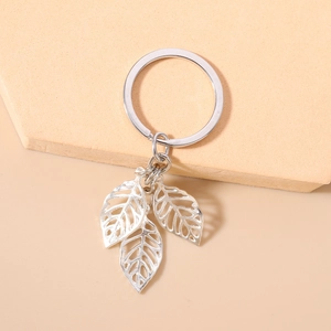 Close-up of bright silver hollow leaf pendants on a leaf-shaped keychain on beige base