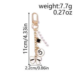 Detailed close-up of golden keychain with black clover, pearl bow, and number five charm