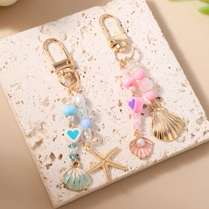 Starfish and shell beaded keychain with heart charms and pearls on stone surface