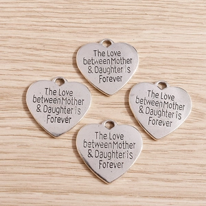 Macro shot of silver matte heart pendants with Mother Daughter engraving on wood