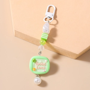Detail of green Good Luck keychain with striped beads and faux pearls on a block