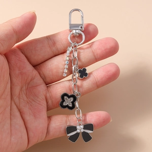 Detail showing clover charms and pearl bow on a silver keychain held by a hand