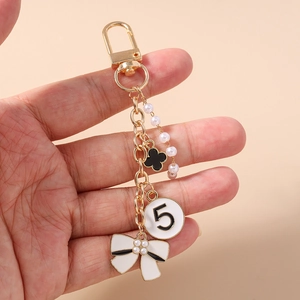Detailed macro view of golden keychain with enamel bow, clover charm, and faux pearls