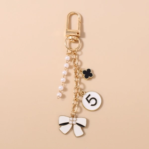 Detail of gold keychain with white pearls, black clover charm, and elegant bow decoration