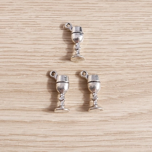 Detailed close-up of three antique silver wine goblet pendants on a light wood background