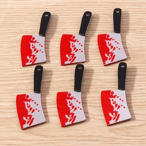 Flat lay of blood-stained acrylic cleaver charms on a light wooden background