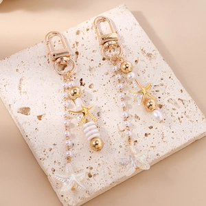 Detailed view of nautical pearl starfish charms with gold hardware on a beige stone base