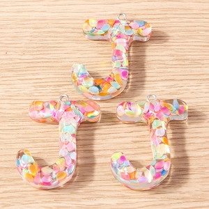 Close-up of three J-shaped colorful resin alphabet charms with iridescent sequins and rings