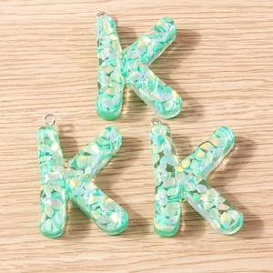 Macro detail of three letter K pendants made of resin with mint green iridescent sequins