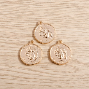 Detailed view of three golden irregular coin charms with embossed portraits on wood background