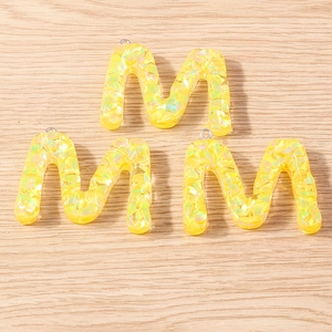 Close-up of three yellow resin letter M pendants with glitter on a wooden surface