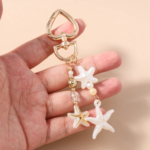 Detail of a gold heart clasp keychain with starfish charms and elegant pearl beads