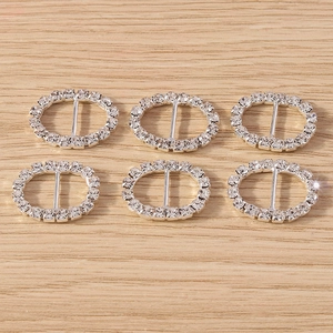 Close-up of six silver oval rhinestone ribbon buckles on a light wooden background