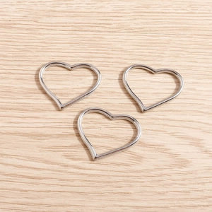 Tre ciondoli a cuore d'argento su legno chiaro per la creazione di gioielli fai-da-te