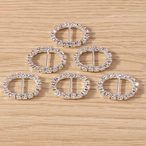Close-up of six oval silver rhinestone buckle sliders on a light wood background