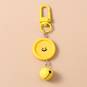 Détail d'un porte-clés jaune avec visage souriant, mousqueton et petite cloche assortie