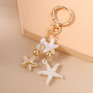 Detail of star keychain with white resin starfish, pearls, and golden hardware hooks