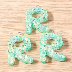 Macro view of mint green resin letter R pendants with iridescent flakes for DIY jewelry