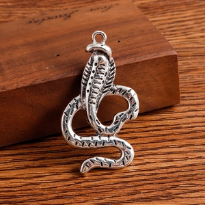 Detailed view of silver-toned cobra pendants with scale texture on dark wood background
