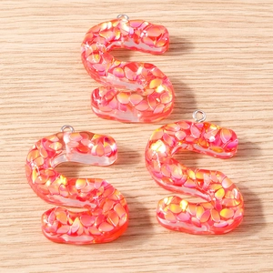 Detailed macro view of S-shaped resin letter pendants with vibrant pink orange glitter