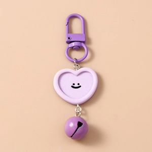 Détail d'un porte-clés cœur violet avec visage souriant, clochette et crochet métal