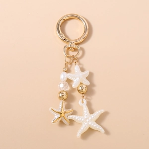 Detail view of starfish keychain with faux pearls and golden accents on a warm beige base