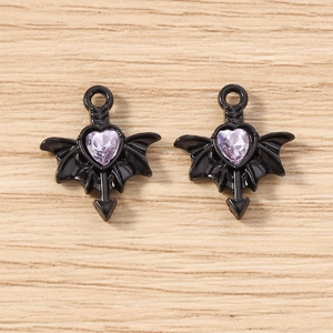 Detailed macro view of gothic black bat wing heart charms with purple gems on wood surface