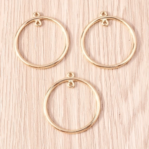 Three gold geometric round pendants for DIY jewelry making on a pink wood background