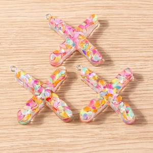 Close-up of X-shaped colorful resin letter charms with iridescent glitter and metal loops