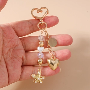 Détail d'un porte-clés coeur doré avec des perles et un pendentif fleur tenu à la main