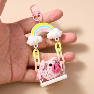 Close-up of a crochet pink pig on a white swing with rainbow and cloud bag pendant