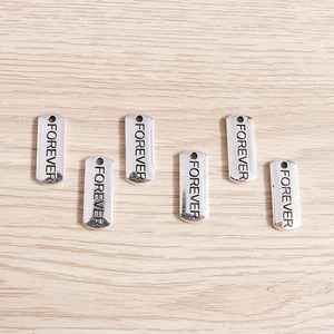 Detailed close-up of rectangular silver pendants with Forever engraving for DIY jewelry making