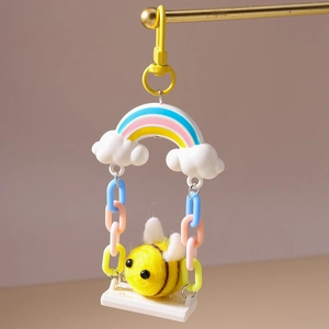 Detail of a plush bee keychain with a colorful chain and rainbow pendant on a display stand