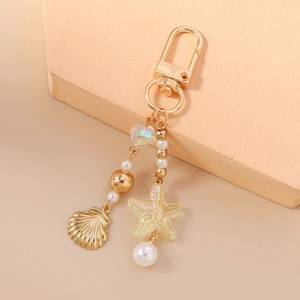 Detail of gold keychain with white pearls, metallic seashells, and iridescent heart charms