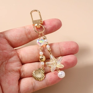 Detail of beaded keychain with gold shell and heart charm held in hand to show scale