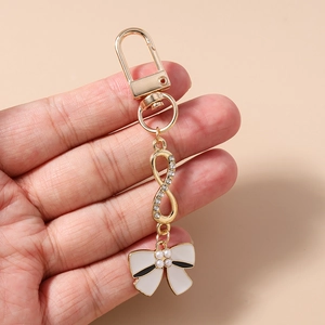 Detail of gold metal keychain with infinity symbol, white bow pendant and pearls