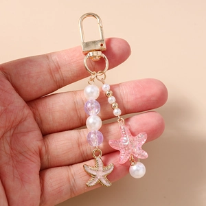Detail view of pearl and starfish beaded keychain with golden metal clasp and charms