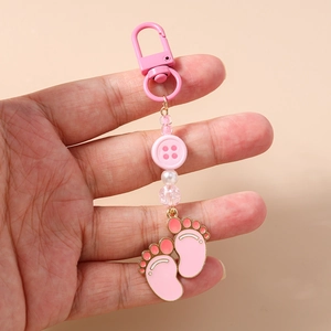 Detail showing pink enamel paw charms and beaded keychain held in hand for scale