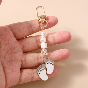 Detail of beaded keychain with double white paw print charms and golden metal clasp