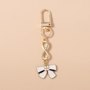 Close-up of golden keychain with infinity symbol, white bow, and faux pearls detail