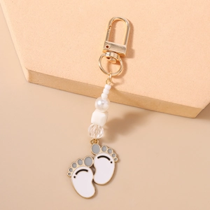Close-up of golden footprint keychain with white enamel charms and beaded tassels